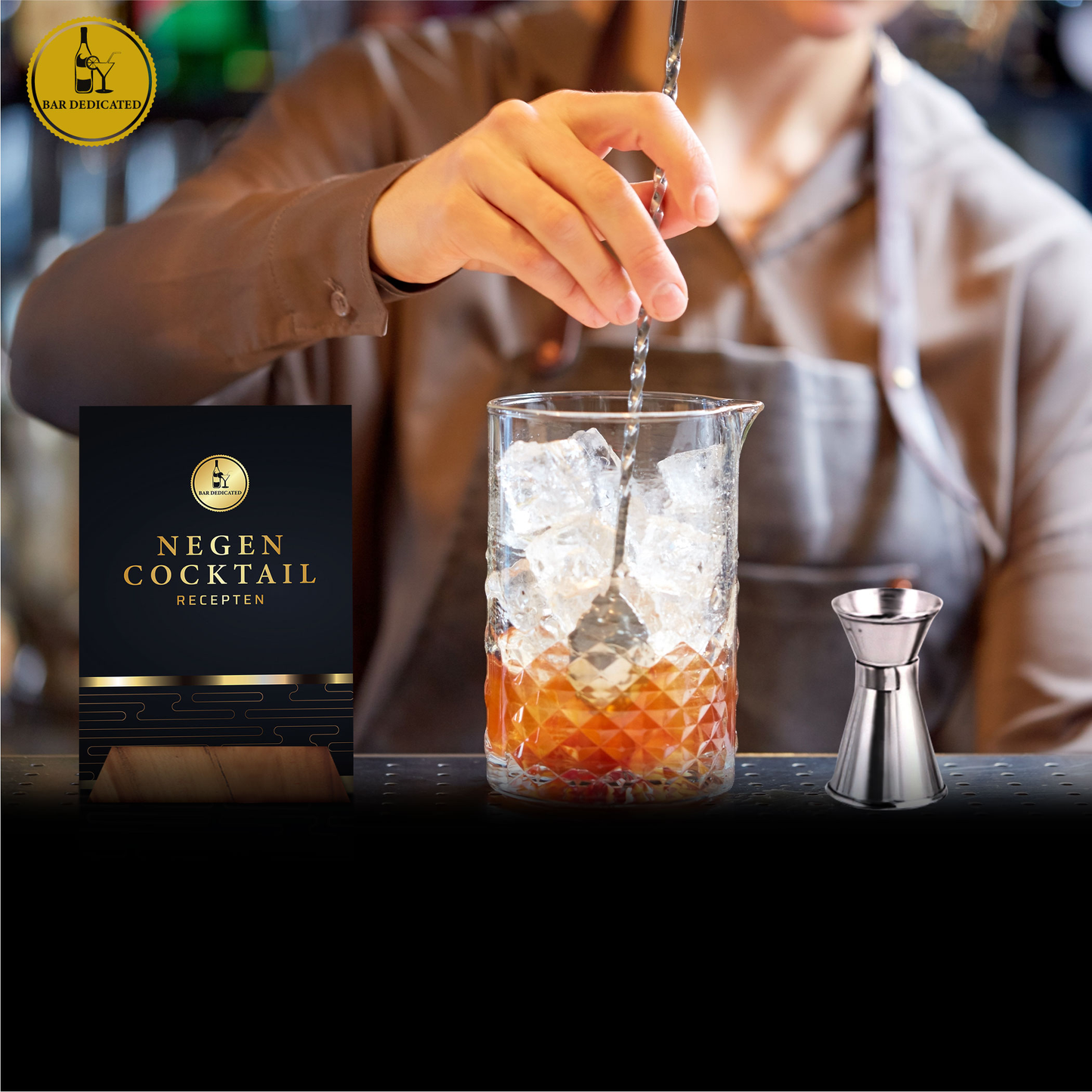 “Bar Dedicated cocktailset zilver – cocktail wordt geroerd met barlepel naast receptenboek ‘Negen Cocktail Recepten’.”